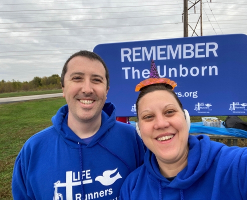 Two people taking picture in front of sign.