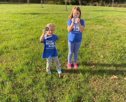 Two children showing off running medals in field.